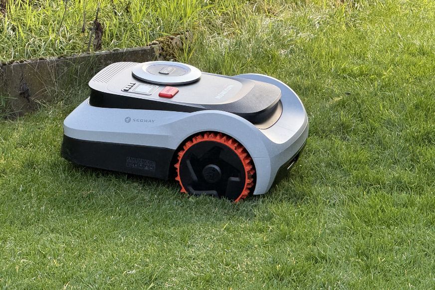 Segway Navimow i210 LiDAR Pro Mähroboter mit orangefarbenen AWD-Rädern mäht eine Böschung entlang einer Rasenkante